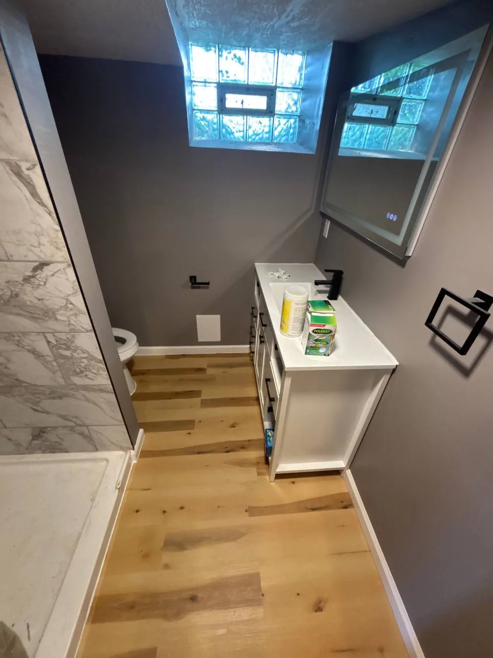 Bathroom after renovation with wood-look flooring, a white vanity, black faucet, and finished baseboards.