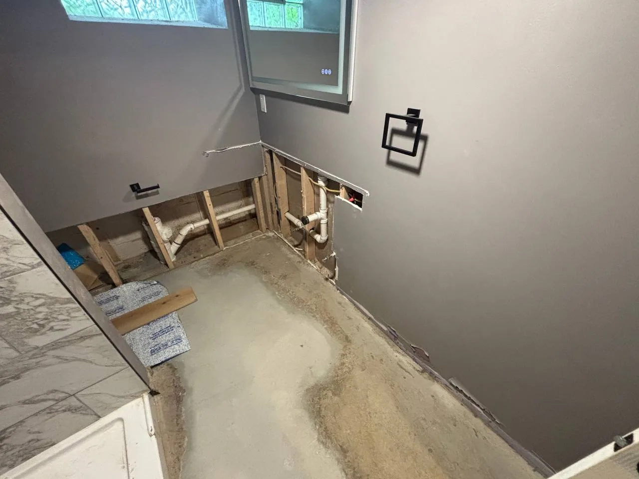 Bathroom before renovation with removed lower wall sections, exposed plumbing, and unfinished floor.